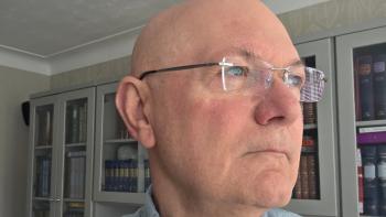 A man in glasses looking to the right, in a contemplative way