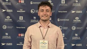 A man in a lanyard smiling, in front of a board covered in logos
