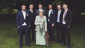 A woman standing in an outdoor setting, with six men standing behind her, all smiling and in wedding outfits
