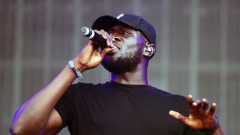 A man in a baseball cap holding a microphone to his mouth.