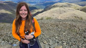 A woman in hiking gear standing on a mountain and smiling