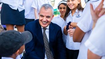 A man in a suit, smiling, surrounded by schoolchildren