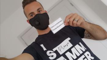 A man in a face mask holding up a card that says 'I have a stammer. Please be patient'