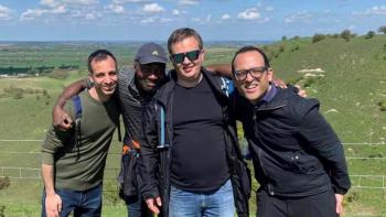 Four men in an outdoor setting crowding together and smiling at the camera