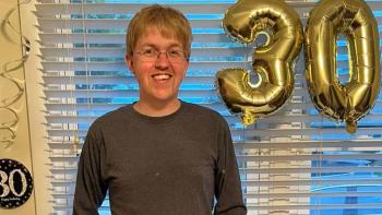 A man smiling, next to balloons in the shape of the number 30