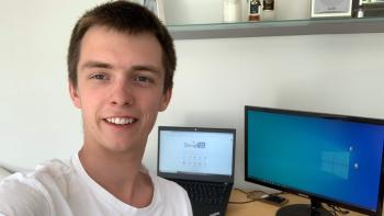 A man smiling in front of two computer screens on a desk