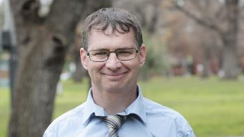 A man in a shirt and tie smiling in a park