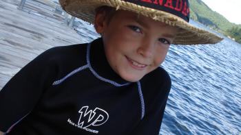 A young boy wearing a straw hat sitting on a jetty