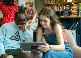 A young man sitting next to a young woman who is holding a tablet which they are both looking at