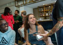 A young man and woman in a cafe looking at a waitress and holding a mobile phone to a card reader