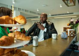 A man at a coffee shop counter talking to a woman obscured by a display of croissants