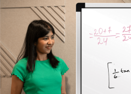A woman holding a pen and standing beside a whiteboard which has writing on it