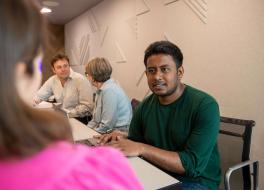 A man sitting at a desk speaking to a woman sitting opposite, whose face we can't see