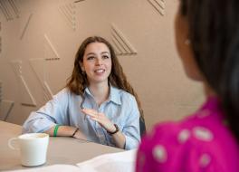 A woman sitting at a desk speaking to a woman sitting opposite whose face we can't see