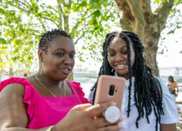 A mother with her daughter, both looking at a phone the mother is holding