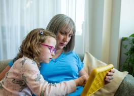 A mother and young daughter sitting on a sofa and looking at a tablet