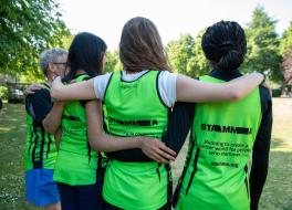 A man and three women in running vests linking arms with their backs to the camera