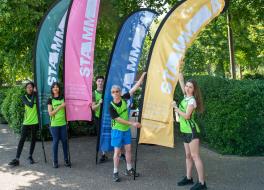 Three women and two men in running outfits holding large flags and looking at the camera