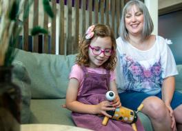 A young girl on a sofa holding a toy, with her mother sitting next to her