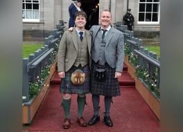 Two men in kilts standing together, looking at the camera and smiling