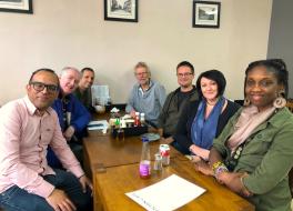 Seven people sitting around a cafe table smiling for the camera