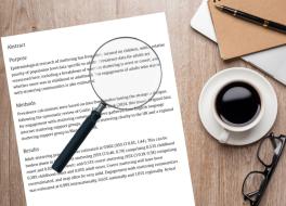 A piece of paper on a desk with text on it. On top of the paper is a magnifying glass, and a cup of coffee is next to it