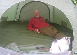 A man lying inside a tent, with a cat in front of him