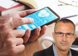 A man's face, in front of a hand using a smartphone