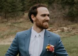A man in a wedding suit looking to the right and smiling