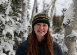 A young woman smiling against a snowy forest scene