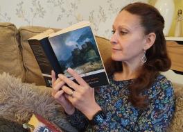 A woman on a sofa reading a paperbook book, with another hardback book on her lap