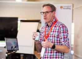 A man wearing a lanyard standing and doing a presentation
