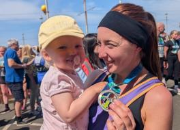 A mother in running gear cuddling her baby daughter and holding up a medal