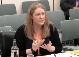 A woman sitting in a meeting room, gesticulating with her hands