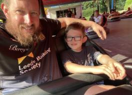 A man and his son sitting in a bumper car and smiling