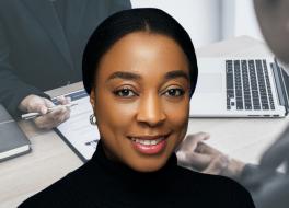 A woman smiling with a background scene of a job interview in progress