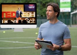 A man on a sports pitch holding a clipboard, with a tv screen showing the man doing a public talk