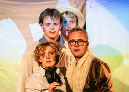 Four actors huddled together on a stage and looking at the camera, in character
