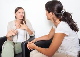 Two women sitting and talking, with one gesticulating with her hands