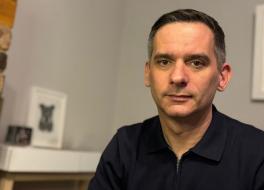 A man looking serious, in front of a living room mantlepiece