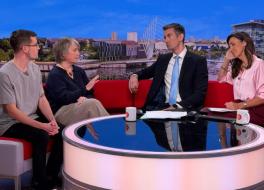 Four people sitting on a sofa in a tv studio, a man and a woman on the left, speaking to another man and woman on the right