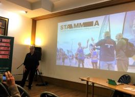 A woman standing in front of a projected screen, presenting to an audience