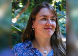 A woman smiling and looking to the right, in front of a tree