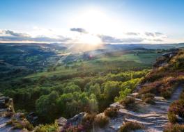 An aerial view of the hills and valleys of the Peak District in Derbyshire, with the sun peaking through clouds