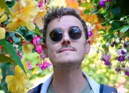 A man wearing sunglasses, standing amid brightly coloured flowers 