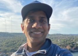 A man smiling, with a backdrop of trees and a horizon