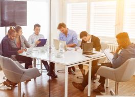 A group of people sitting round a table in a work setting, each one looking at laptops or tablets