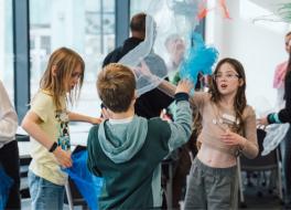 Three children playing with pieces of fabric, waving them through the air