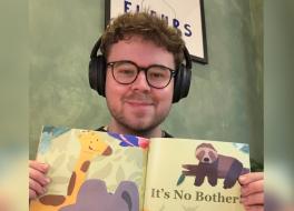 A man wearing headphones and holding up a children's book