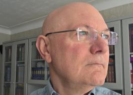 A man in glasses looking to the right, in a contemplative way